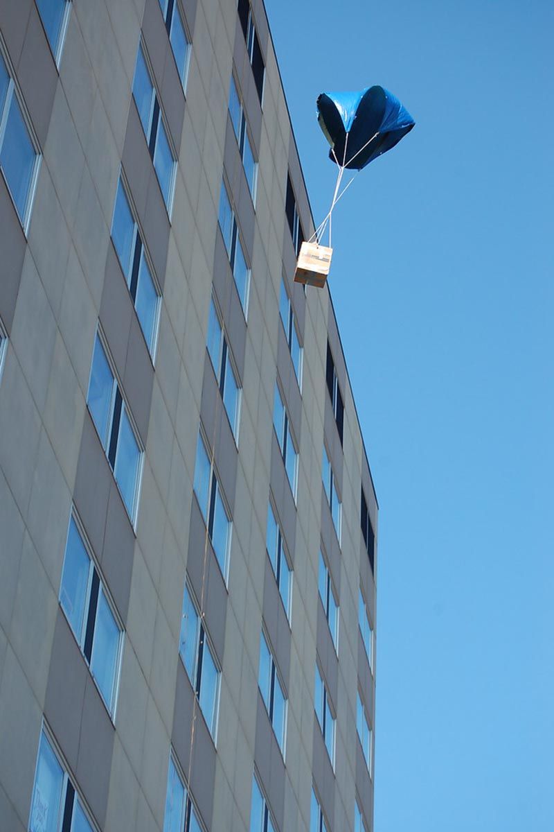 A packaged pumpkin with a parachute falling from the Engineering Sciences Building